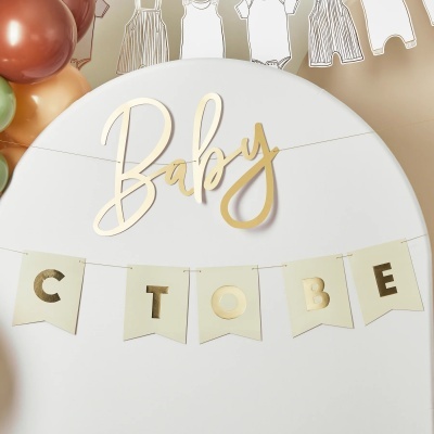 Decoração de festa de chá de bebé com letras douradas, faixa de papel em creme e dourado, balões coloridos e guirlanda de roupas de bebé em papel
