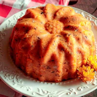 Bolo laranja com pontinhos escuros em prato branco e flores laranjas