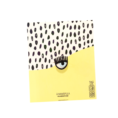 Broche em forma de olho fixado num suporte decorativo amarelo e branco com padrão de pontos