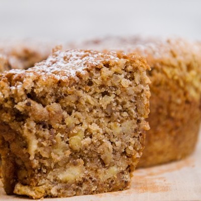 Três muffins castanhos com pedaços de nozes e açúcar em pó sobre madeira clara