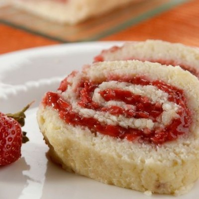 Dois pedaços de bolo enrolado com recheio vermelho e um morango inteiro num prato branco