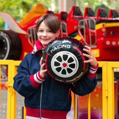 Criança com balão em forma de roda com texto RACING no parque de diversões