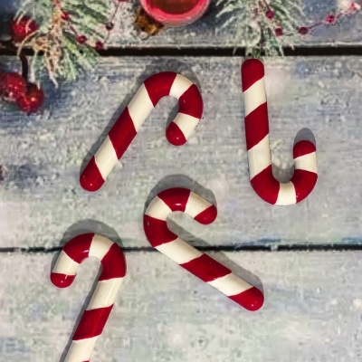 Bengalas de Natal vermelhas e brancas com padrão às riscas sobre superfície de madeira decorada com motivos natalícios.