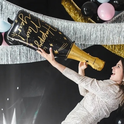 Mulher segurando balão gigante de champanhe com decoração festiva ao fundo