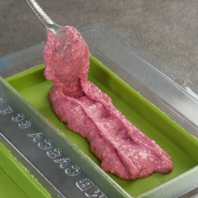 Pasta rosada com sementes em recipiente verde e transparente, mexida com colher