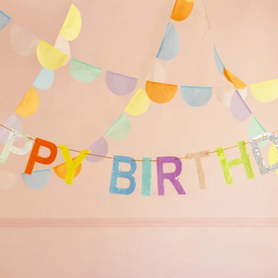 Guirlanda colorida com letras HAPPY BIRTHDAY penduradas numa parede cor rosa