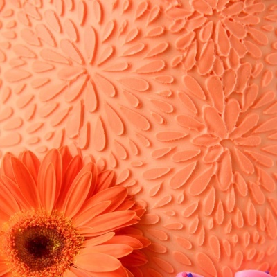 Flor de gerbera laranja sobre superfície com padrão floral em relevo alaranjado.