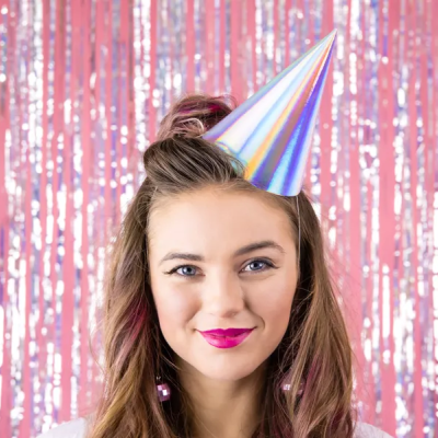 Mulher com chapéu de festa prateado e cortina metálica cor-de-rosa ao fundo