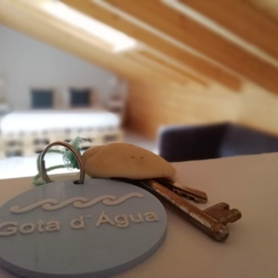 Chave com pendente azul 'Gota d'Água' em primeiro plano com quarto desfocado ao fundo
