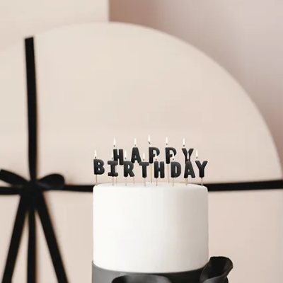 Bolo branco com velas HAPPY BIRTHDAY e laço preto, fundo com embrulho redondo e fita preta