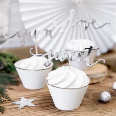 Cupcakes com cobertura branca e toppers prateados em letras cursivas, decorados com estrelas e elementos prateados sobre madeira.