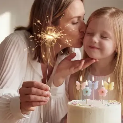 Bolo de aniversário branco com velas de flores e borboletas, mulher segurando vela de fogo de artifício em forma de 5 e criança loira