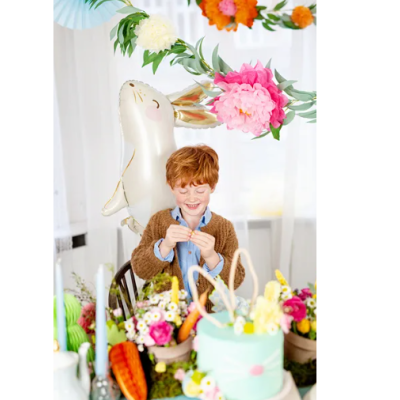 Criança sorridente segurando ovo da Páscoa em mesa decorada com bolo e flores