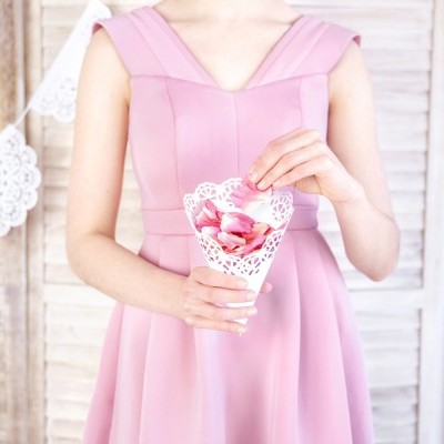 Mulher com vestido rosa segurando cone rendado com pétalas cor de rosa