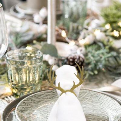 Mesa posta com prato decorativo cinza e guardanapo branco com suporte de metal dourado em forma de galhos