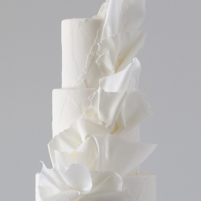 Bolo branco de três andares com decoração branca abstrata em fundo cinzento claro