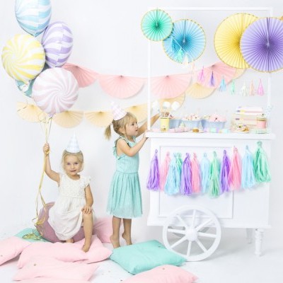 Carrinho de festa branco com pompons coloridos e duas meninas numa festa com balões e decoração pastel