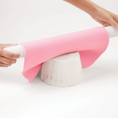 Rolo branco esticando faixa de silicone rosa sobre superfície branca