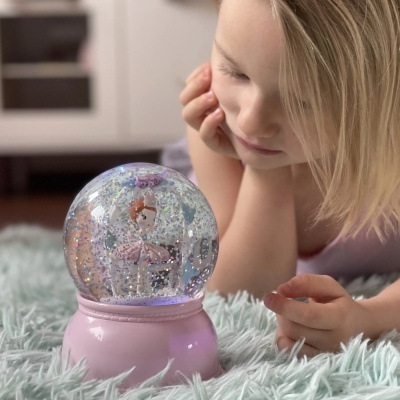 Criança a olhar para globo de neve com bailarina e base rosa sobre tapete felpudo