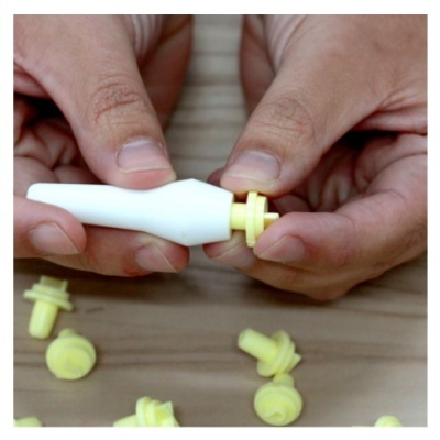 Mãos segurando peças plásticas brancas e amarelas sobre madeira