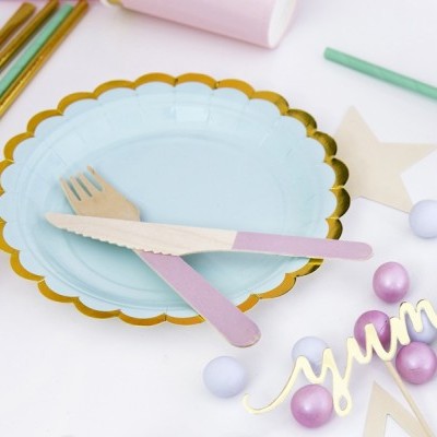 Prato azul claro com borda dourada, talheres de madeira com cabo rosa e decoração festiva ao redor
