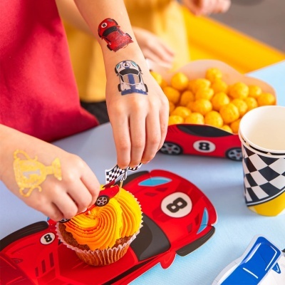 Mãos de criança a decorar cupcake com tatuagens temáticas de carros de corrida e decoração de festa.