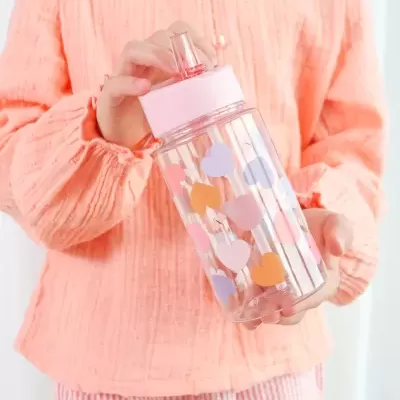 Garrafa de plástico transparente com tampa rosa e corações coloridos, segurada por pessoa com blusa cor de salmão.