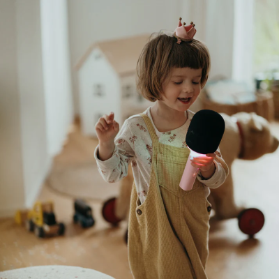 Menina a brincar com microfone rosa e vestir jardineira bege