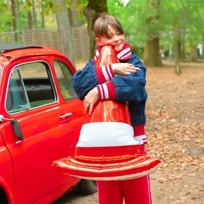 Criança com balão de cone de trânsito e carro vermelho num parque