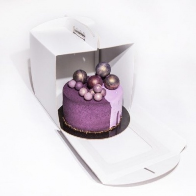 Bolo pequeno roxo decorado com bolinhas brilhantes numa caixa branca aberta