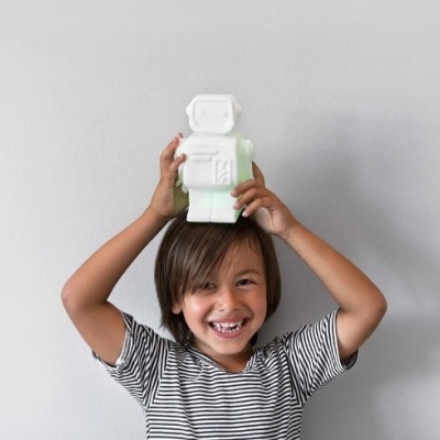 Criança com figura robô de cerâmica branca na cabeça, parede cinzenta ao fundo