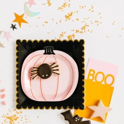 Biscoito decorado de abóbora rosa com aranha preta e decoração temática de Halloween em amarelo e preto.