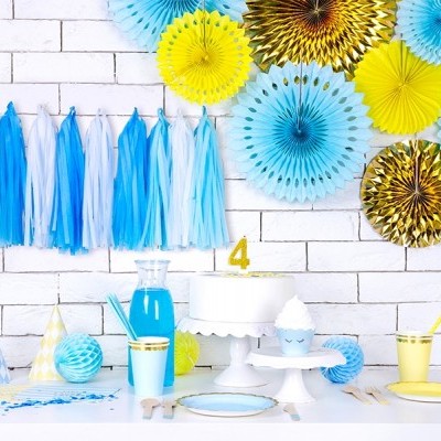 Decoração de festa colorida com pompons de papel, bolo com vela número 4, copos e chapéus de festa sobre mesa branca