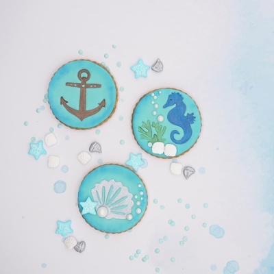 Três biscoitos decorados com motivos marítimos e confeitos coloridos