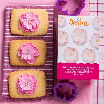 Pacote de cortadores de massa Decora e bolachas decoradas com flores rosas sobre toalhas rosa