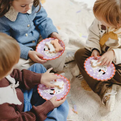 Crianças sentadas com pratos de papel lilás com biscoitos em forma de pessoa