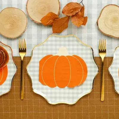 Mesa posta com pratos de vidro, guardanapos de abóbora, talheres dourados e tábuas de madeira decorativas
