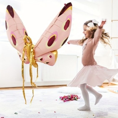 Asas de borboleta rosa com padrões coloridos e fitas douradas, usadas por criança em interior claro