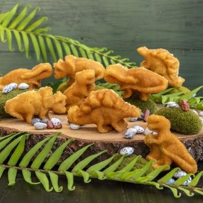 Biscoitos em forma de dinossauros sobre placa de madeira com folhas e pedras