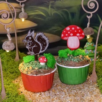Dois cupcakes decorados com esquilo e cogumelos em fundo verde