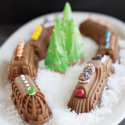 Bolos em forma de comboio castanho com confeitos coloridos sobre base branca com árvores verdes