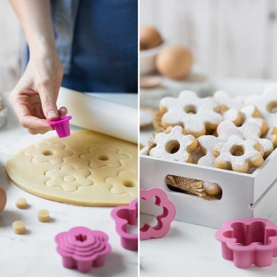 Cortadores de bolachas rosa em forma de flor e bolachas florais polvilhadas com açúcar em pó numa caixa branca