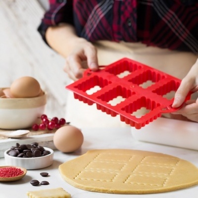 Forma de silicone vermelha para cortar massa com seis quadrados, ovos e massa na bancada branca