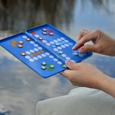 Jogo de tabuleiro portátil azul com peças coloridas e mãos humanas