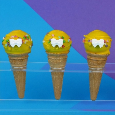 Três gelados amarelos em cones com decoração colorida e osso branco sobre fundo azul e roxo