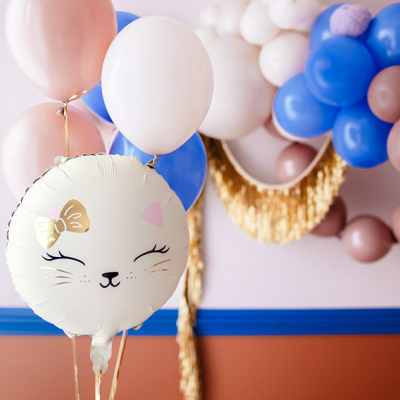 Balão de gato branco com laço dourado rodeado por balões coloridos em ambiente festivo interior