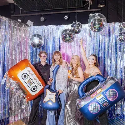 Grupo de quatro pessoas numa festa com balões de objetos musicais e bolas de espelho
