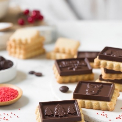 Biscoitos quadrados com chocolate decorados com motivos natalícios sobre superfície branca