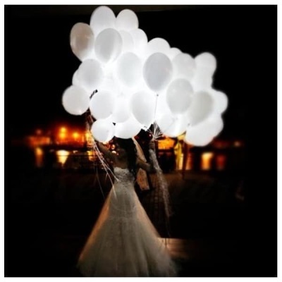 Balões brancos iluminados sendo segurados por duas pessoas em ambiente escuro