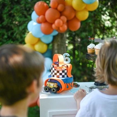 Bolo de aniversário decorado com carros e padrão xadrez, com vela 6, em festa ao ar livre